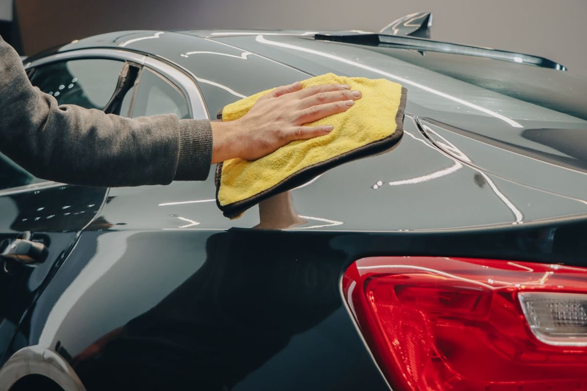 Hand wiping a black car with a microfiber cloth